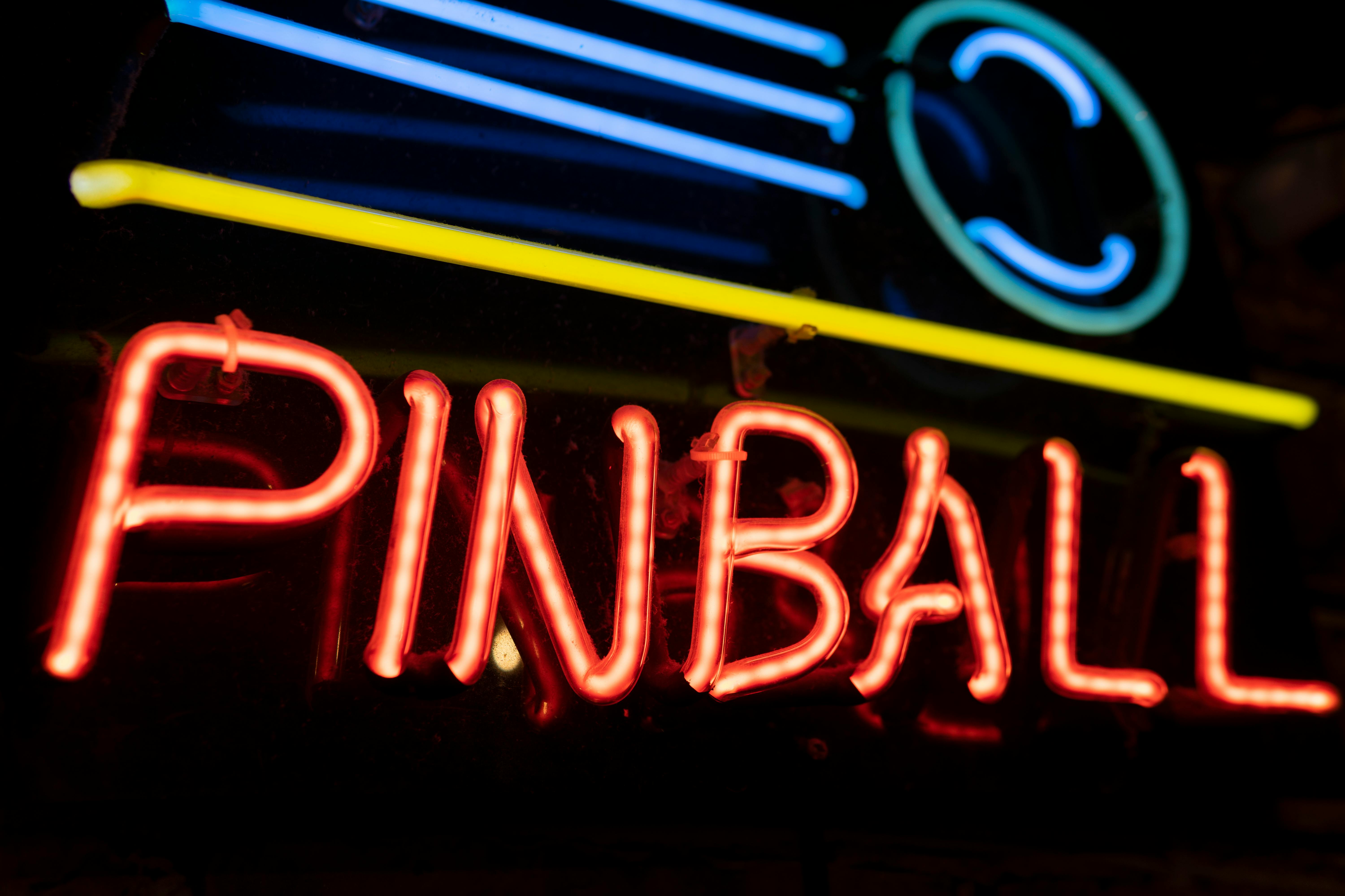 A colorful neon sign illuminating the word 'PINBALL' against a dark background, capturing a retro nightlife vibe.